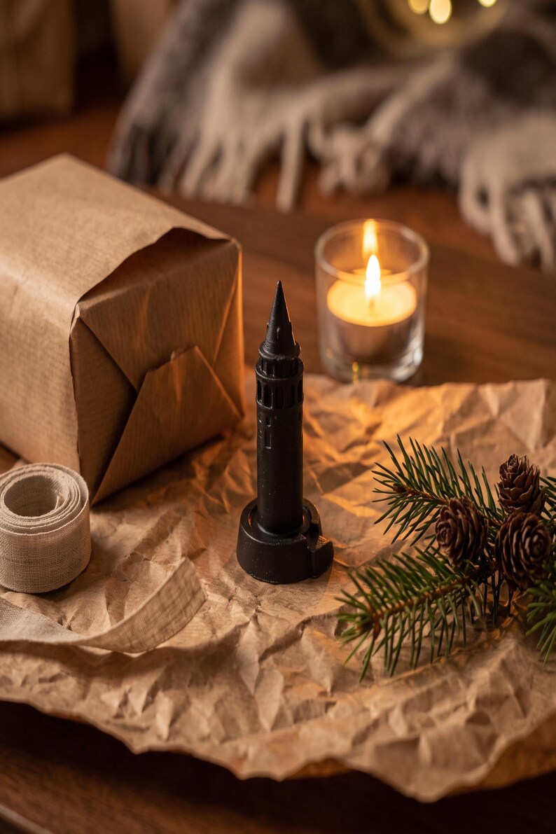 Black finish Galata Tower miniature on crumpled kraft paper beside a wrapped gift, linen ribbon, a candle and a pine sprig