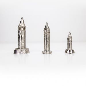 Three polished stainless steel Galata Tower miniatures in small, medium and large sizes standing in a row on a white surface