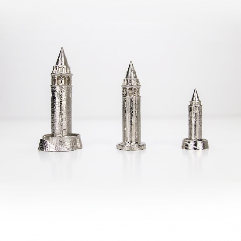 Three polished stainless steel Galata Tower miniatures in small, medium and large sizes standing in a row on a white surface