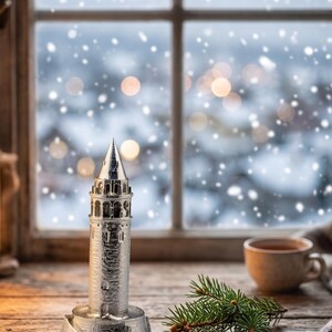 Polished Galata Tower miniature on a rustic window sill with snow falling outside, a cup of tea and a pine branch