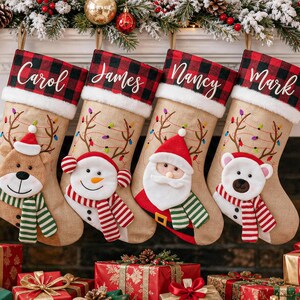 Könnte beinhalten: Vier Weihnachtsstrümpfe aus Jute mit einem rot-schwarz karierten Umschlag, auf dem die Namen Carol, James, Nancy und Mark stehen. Jeder Strumpf zeigt gesticktes Rentiergeweih mit bunten Lichtern und eine Plüschfigur: Bär, Schneemann, Weihnachtsmann und Eisbär.
