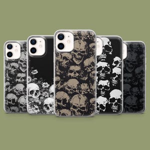 May include: A collection of five phone cases with skull designs. The cases feature various skull patterns in black, white, and tan, with one case showcasing white flowers. The cases are displayed against a muted green background.