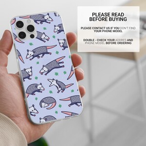 May include: A clear phone case with a light blue background and a repeating pattern of gray opossums with pink noses and white bellies. The case has a camera cutout for an iPhone.