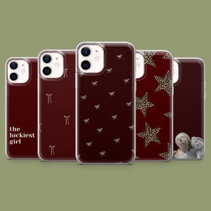 Może przedstawiać: Kolekcja etui na telefony o różnych wzorach. Etui mają ciemnoczerwone tło z białymi wzorami kokardek, wzorami gwiazd i tekstem "the luckiest girl". Etui są przeznaczone do smartfona.