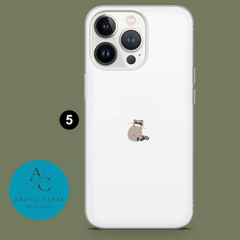 May include: White iPhone case with a clear back and a raccoon illustration. The case has a raised camera bump with three black camera lenses.