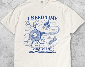Könnte beinhalten: Cremefarbenes T-Shirt mit einer blauen Darstellung eines Neurons und dem Text "I NEED TIME TO RESTORE MY neurotransmitters." Das Diagramm enthält Beschriftungen für Zellteile. Das T-Shirt hat einen Rundhalsausschnitt und kurze Ärmel.