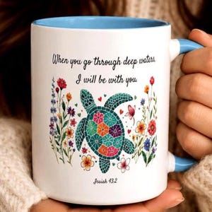 May include: White ceramic mug with a blue interior and handle. The mug features a colorful sea turtle design surrounded by flowers and the text "When you go through deep waters, I will be with you. Isaiah 43:2."