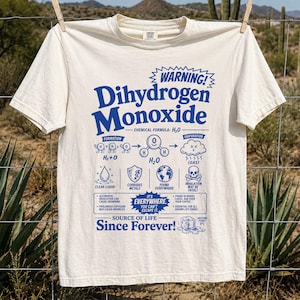 以下が含まれることがあります： オフホワイトのTシャツで、青いグラフィックのテキストとイラストがプリントされています。デザインには「Dihydrogen Monoxide」という警告、化学式、そしてドクロのシンボルを含む水の特性を示す様々なアイコンが含まれています。