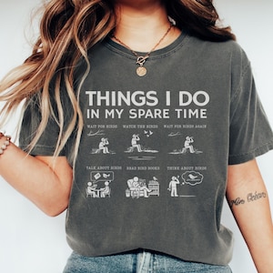 Puede incluir: Camiseta gris oscuro con el texto "THINGS I DO IN MY SPARE TIME" e ilustraciones de actividades de observación de aves. El diseño incluye frases como "Esperar a los pájaros" y "Hablar de pájaros."