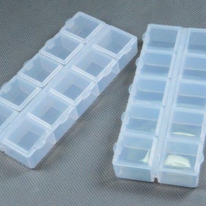 May include: Two rectangular storage organizers made of translucent, semi-clear plastic. Each organizer features ten individual square compartments arranged in two parallel rows of five, with each compartment having its own hinged lid.