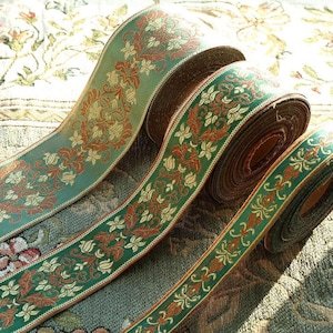 Peut inclure: Trois rouleaux de ruban en tissu tissé présentant un motif floral répétitif dans des tons de vert sauge, orange rouille et crème. Ce ruban décoratif affiche des motifs botaniques complexes avec des dessins symétriques de feuilles et de fleurs.