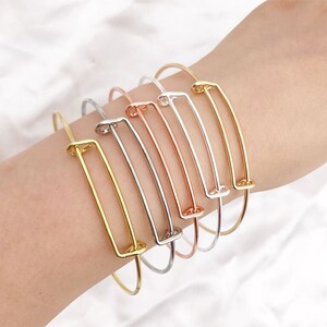 May include: A set of five expandable bangle bracelets in gold, silver, and rose gold. Each bracelet features a rectangular open space.