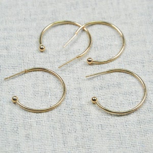 Può includere: Tre paia di orecchini a cerchio dorati con piccoli accenti a sfera. I cerchi sono di dimensioni diverse.