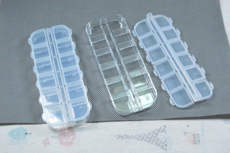 Peut inclure: Trois piluliers en plastique transparent. Chaque organisateur comporte plusieurs petits compartiments pour ranger des pilules ou de petits objets. Les organisateurs sont rectangulaires avec des bords arrondis.