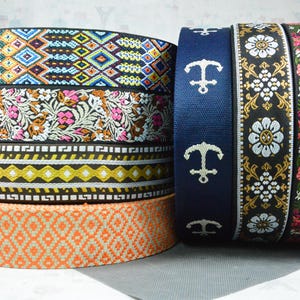 Könnte beinhalten: Ein Stapel dekorativer Bänder mit verschiedenen Mustern. Designs umfassen geometrische, florale und nautische Themen. Die Farben reichen von Orange, Blau und Schwarz bis hin zu Weiß, Gelb und Rosa. Die Bänder werden wahrscheinlich zum Basteln oder Verzieren verwendet.