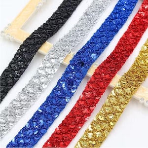 May include: Close-up of several rows of sequin trim in various colors. The colors include black, silver, blue, red, and gold. The trim is made of small, round sequins sewn onto a fabric backing. The sequins are shiny and reflect light.