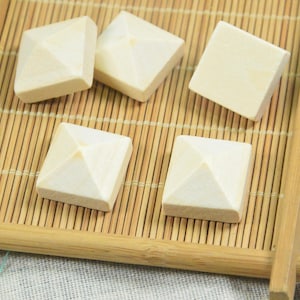May include: Five wooden pyramid-shaped blocks in a square shape, arranged on a bamboo mat in a wooden tray. The blocks are a light beige colour.