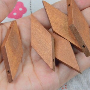 May include: A collection of four diamond-shaped wooden beads with a natural brown finish. Each bead features a smooth, flat surface and a single drilled hole at the top and bottom, allowing for stringing. The wood grain is visible throughout.
