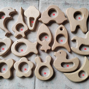 May include: A set of 14 wooden teethers in various shapes, including a dolphin, ice cream cone, car, tooth, rocket, fish, heart, rocking horse, duck, moon, flower, bunny, and star. The teethers are all made of natural wood and have a smooth, polished finish.