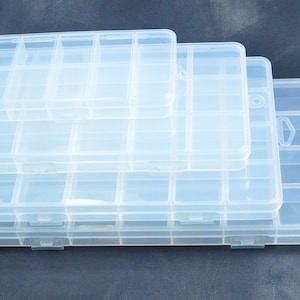 Könnte beinhalten: Ein Stapel aus vier rechteckigen, transparenten Kunststoff-Aufbewahrungsboxen mit mehreren Innenfächern. Jeder Behälter verfügt über einen Klappdeckel mit einem sicheren Verschlussmechanismus, der einen klaren Blick auf den Inhalt bietet.
