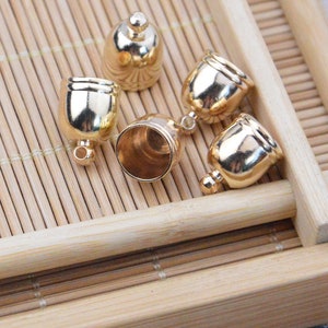 May include: Five gold-toned metal end caps for cords or jewelry. The caps have a rounded top and a small loop at the bottom.
