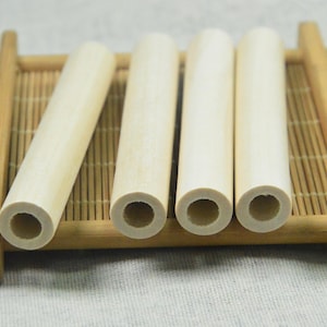 Op de afbeelding: Vier natuurlijke houten pinnen met een holle kern, gerangschikt op een bamboemat. De pinnen zijn ongeveer 25 cm lang en 2,5 cm in diameter.