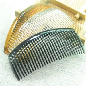May include: Two hair combs, one black and one translucent brown, are arranged on a white surface. The black comb is in the foreground and the brown comb is behind it. Both combs are curved and have a row of teeth.