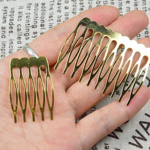 Op de afbeelding: Twee goudkleurige metalen haar kammen. Elke kam heeft een reeks tanden en een decoratieve geschulpte rand. De kammen worden in een hand gehouden, die hun grootte en ontwerp laten zien. Deze haaraccessoires zijn ideaal voor knutselen.