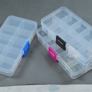 May include: Several clear plastic storage boxes with multiple compartments. One box has a blue clasp, while others have pink and black clasps. The boxes are designed for organizing small items like beads or jewelry.