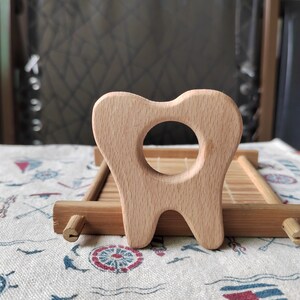 May include: A wooden teether shaped like a tooth, with a hole in the middle for a baby to hold and chew on. The teether is made of natural wood and is a safe and healthy option for babies.
