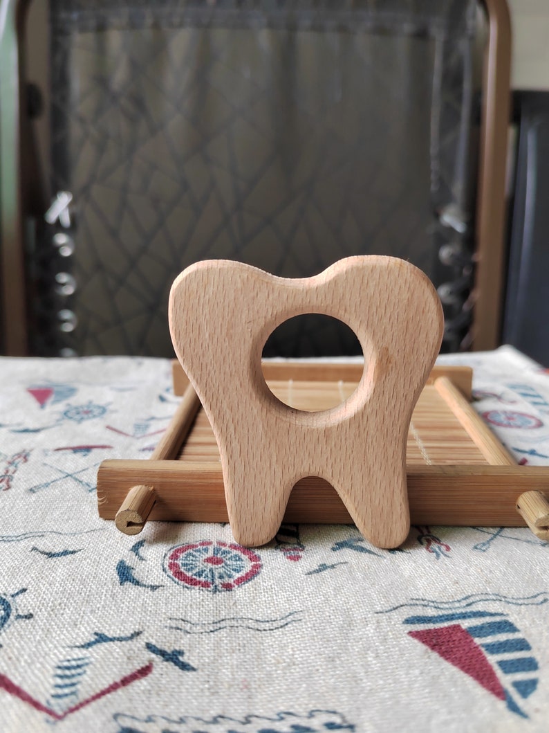 May include: A wooden teether shaped like a tooth, with a hole in the middle for a baby to hold and chew on. The teether is made of natural wood and is a safe and healthy option for babies.