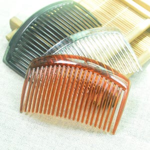 May include: Three plastic hair combs in different colors: black, clear, and brown. The combs are stacked on top of each other.