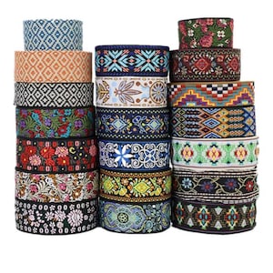 May include: A collection of decorative ribbon rolls with diverse patterns and colours. The ribbons display geometric, floral, and abstract designs in blue, orange, black, green, red, and yellow. The rolls are stacked against a white backdrop.