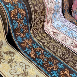 Könnte beinhalten: Nahaufnahme von mehreren Rollen dekorativen Bandes. Die Bänder weisen florale Muster in verschiedenen Farben auf, darunter Braun, Gold, Blau und Rosa. Die Bänder werden wahrscheinlich für Bastelarbeiten, Nähen oder Geschenkverpackungen verwendet.