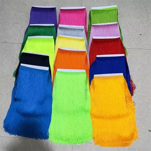 May include: A collection of fringe trim strips arranged in multiple rows, featuring a wide variety of vibrant colours including neon green, bright blue, yellow, orange, red, purple, pink, and black, each attached to a white header tape.