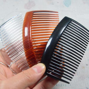 May include: A set of three hair combs featuring a curved design with multiple teeth. The combs are made of smooth plastic in three distinct colors: one transparent clear, one translucent amber brown, and one solid opaque black.