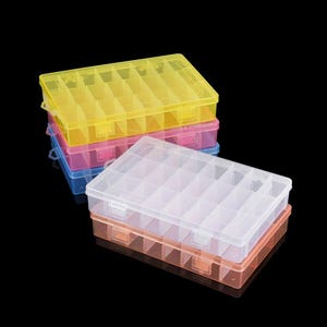 Könnte beinhalten: Stapel bunter Kunststoff-Aufbewahrungsboxen. Die Boxen sind in mehrere Fächer unterteilt, mit einem transparenten Deckel und einer farbigen Basis. Die Farben umfassen Gelb, Rosa, Blau und Orange.
