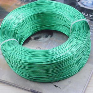May include: A coil of bright green wire, tightly wound and secured with a white band. The wire has a metallic sheen, suggesting it's made of a durable material. This item is likely used for crafting, jewelry making, or other DIY projects.