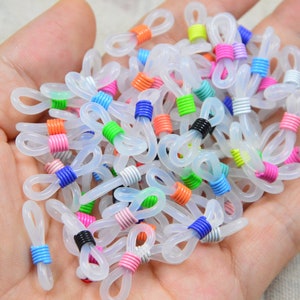 以下が含まれることがあります： カラフルなコイルワイヤーのアクセントが付いた透明なプラスチック製の眼鏡チェーンホルダーの山。ホルダーは、ピンク、ブルー、グリーン、オレンジ、ブラックなど、さまざまな色があります。