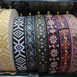 May include: A collection of decorative ribbons in various colors and patterns. The ribbons include geometric and floral designs in shades of beige, yellow, black, green, blue, red, and brown. The ribbons are rolled up, showcasing their intricate details.