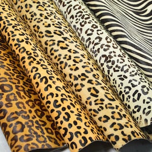 May include: A collection of five animal print hides arranged in overlapping layers. The patterns include various leopard spots in shades of gold, tan, and cream, alongside a black and white zebra stripe pattern on the far right side of the display.