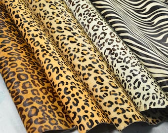 May include: A collection of five animal print hides arranged in overlapping layers. The patterns include various leopard spots in shades of gold, tan, and cream, alongside a black and white zebra stripe pattern on the far right side of the display.