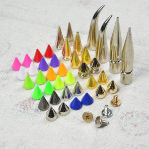 May include: A collection of metal cone studs in various colors and sizes. The studs include silver, gold, and black finishes, as well as vibrant colors like pink, red, and blue. Some studs have a pointed design, while others are rounded.