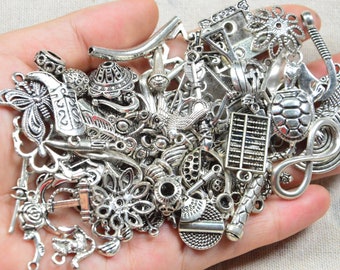 May include: A collection of silver-toned metal charms, including a butterfly, a turtle, a bird, and a flower. The charms are arranged in a pile and are ready to be used for jewelry making or other craft projects.