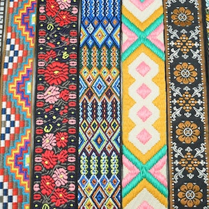 Puede incluir: Siete tiras verticales de cinta tejida decorativa con diversos patrones. Los diseños incluyen diamantes geométricos amarillos, zigzags multicolores, motivos florales rojos sobre negro, redes de diamantes azules, formas rosas y turquesas, y enredaderas.