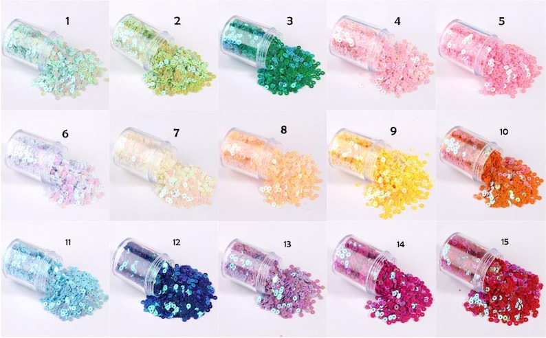 May include: A collection of fifteen small, clear plastic jars, each filled with colorful sequins. The sequins are in various colors, including green, pink, blue, yellow, orange, and purple. The jars are tilted, with sequins spilling out.