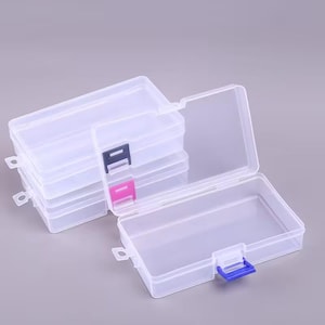 May include: A set of rectangular, clear plastic storage containers with hinged lids. Each container features a small, coloured latch in blue or pink to secure the lid. The boxes are stackable and have a small loop on one side for hanging storage.