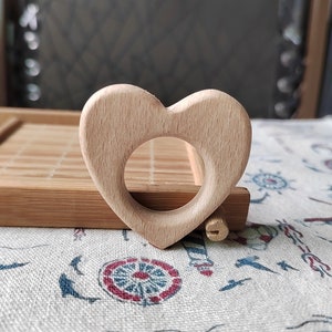 May include: A light brown wooden heart-shaped teether for babies. The teether has a smooth surface and a hole in the center.