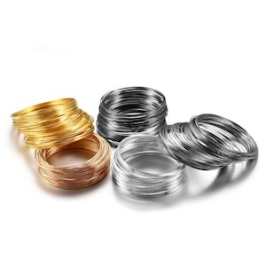 Pode incluir: Uma variedade de bobinas de arame metálico em ouro, cobre, prata e cinza escuro. As bobinas são enroladas e empilhadas, mostrando uma variedade de acabamentos metálicos. Provavelmente usadas para fazer joias ou projetos de artesanato.