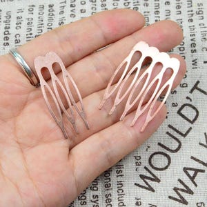 May include: Two copper-colored hair combs with an open, oval design. Each comb has multiple tines and a decorative top. The combs are held in a hand, showcasing their delicate, handcrafted appearance. These hair accessories are ideal for weddings or special occasions.